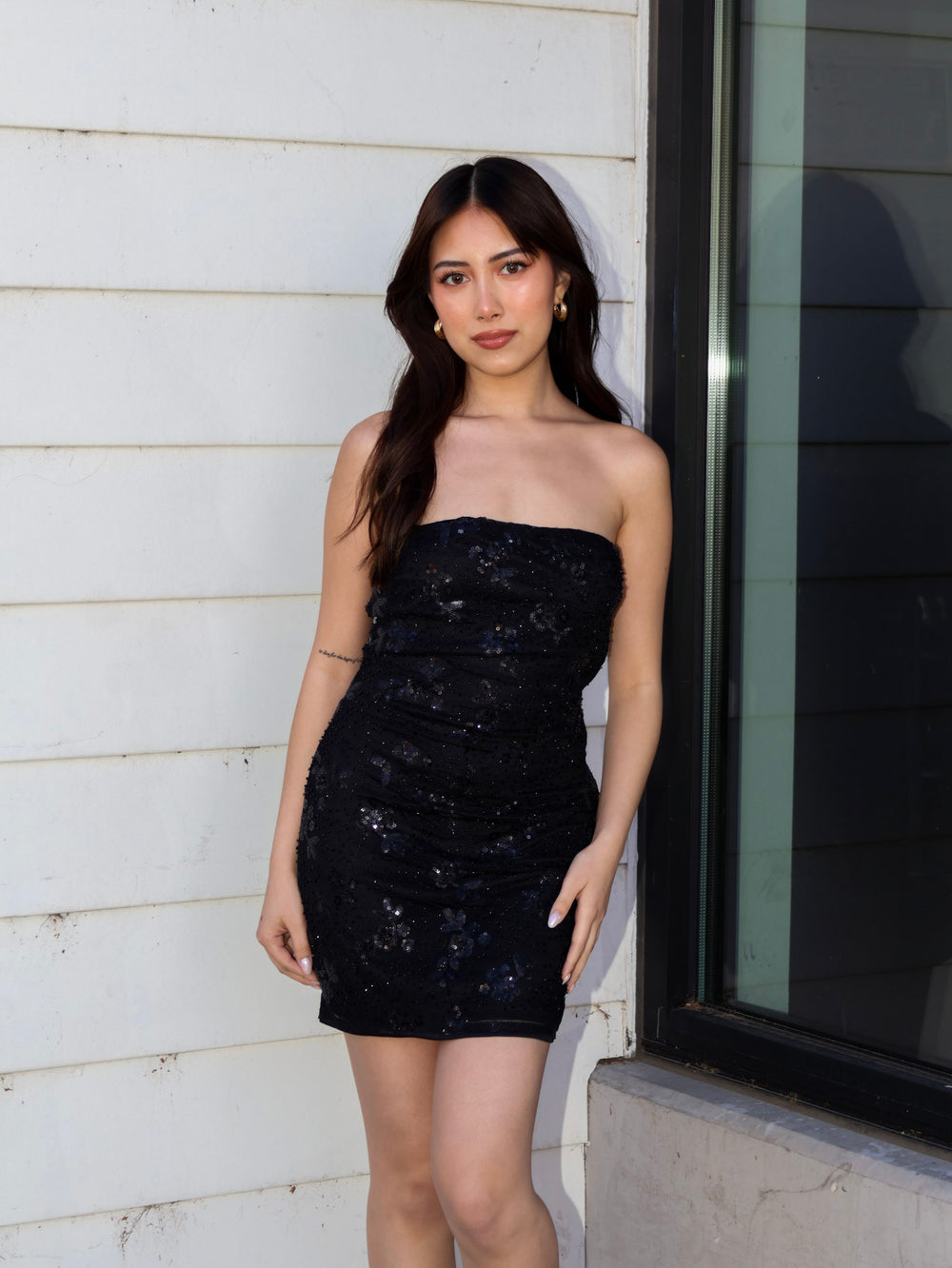 Woman wearing a black sequin dress standing against a light-colored wall.