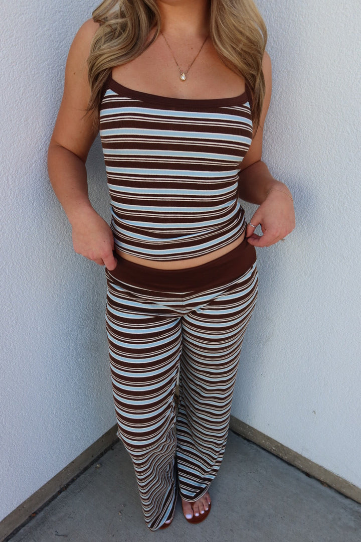 A woman wearing a matching two-piece lounge set with brown, beige, and white horizontal stripes, standing in a corner against a white wall.