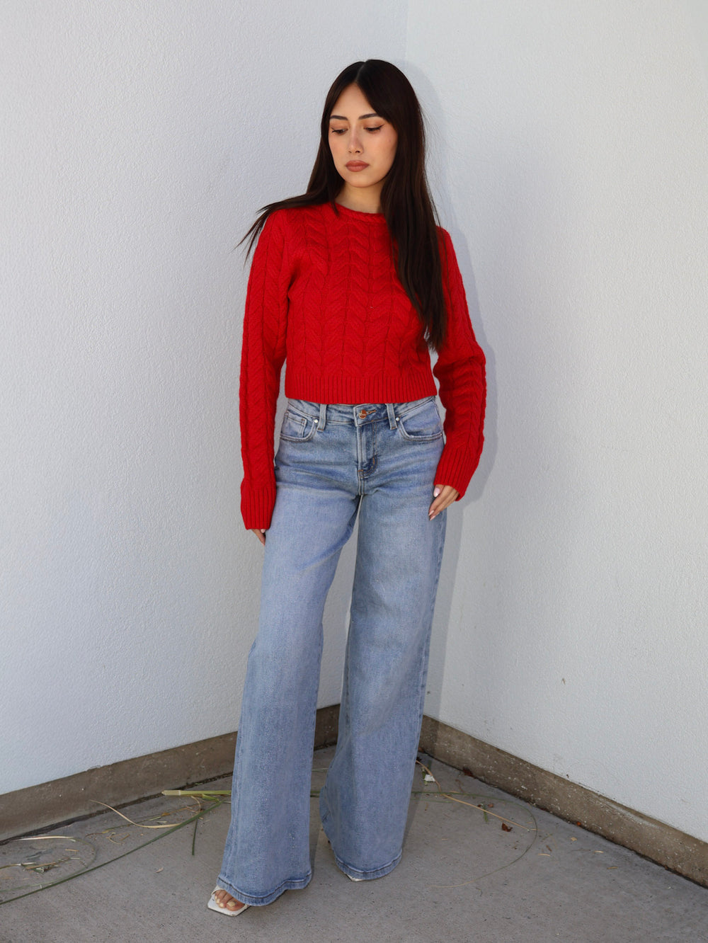 Person wearing a red sweater and blue jeans against a plain white wall.