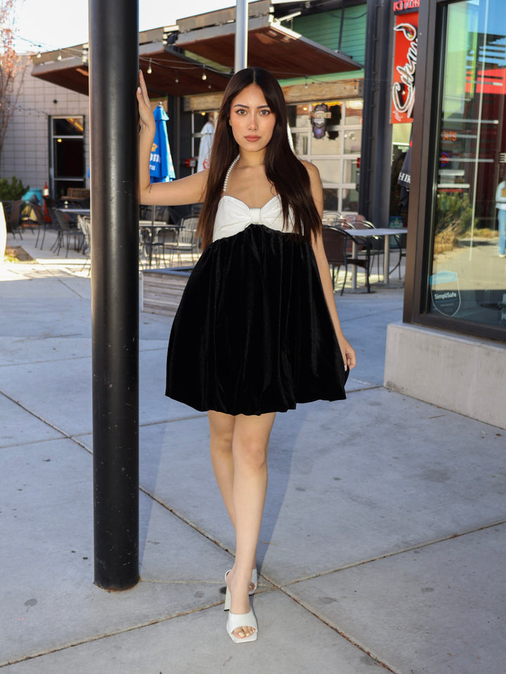 Woman in a black skirt and white top standing on a sidewalk with a building in the background