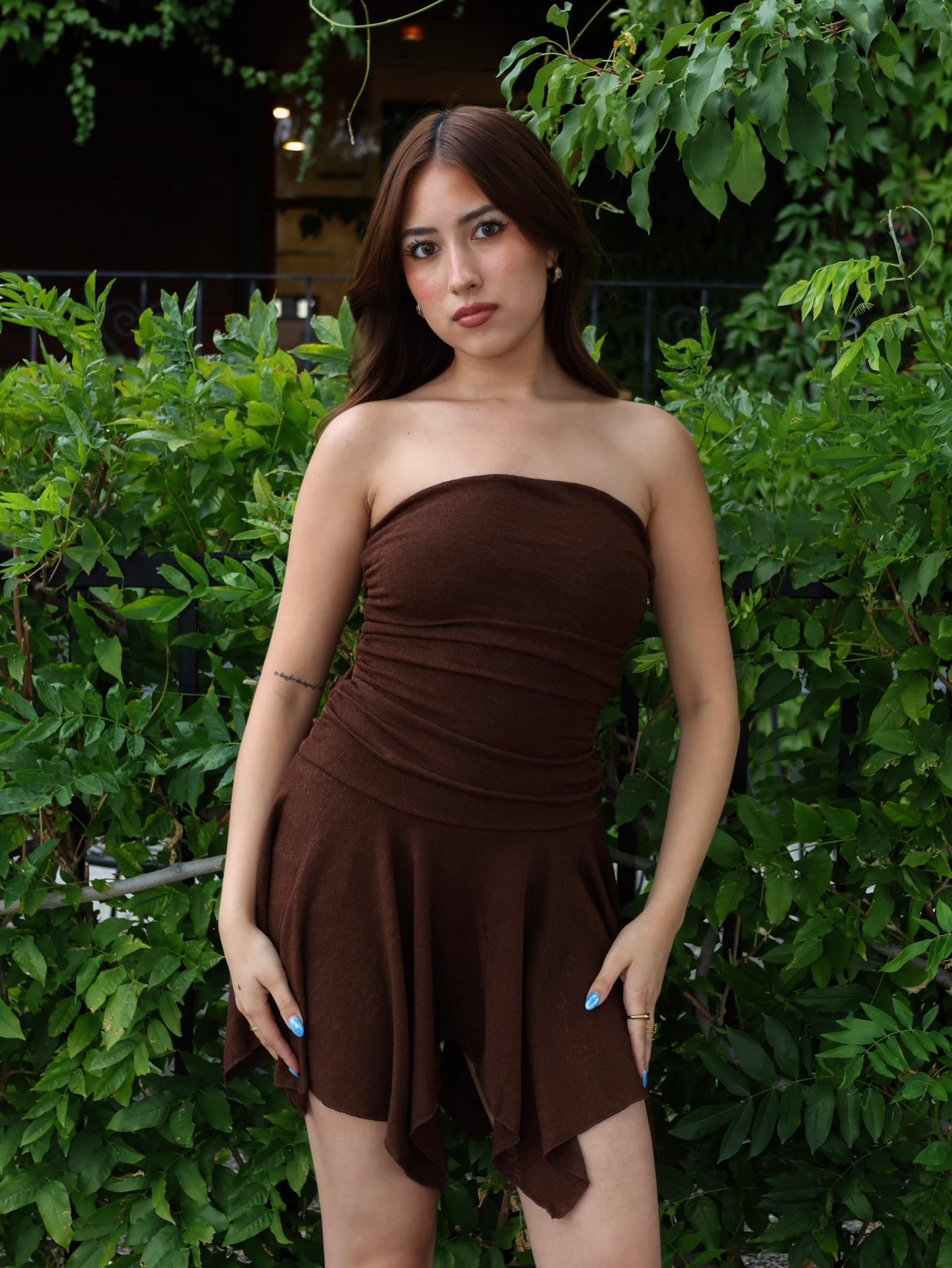 Woman wearing a brown strapless dress standing in front of green foliage