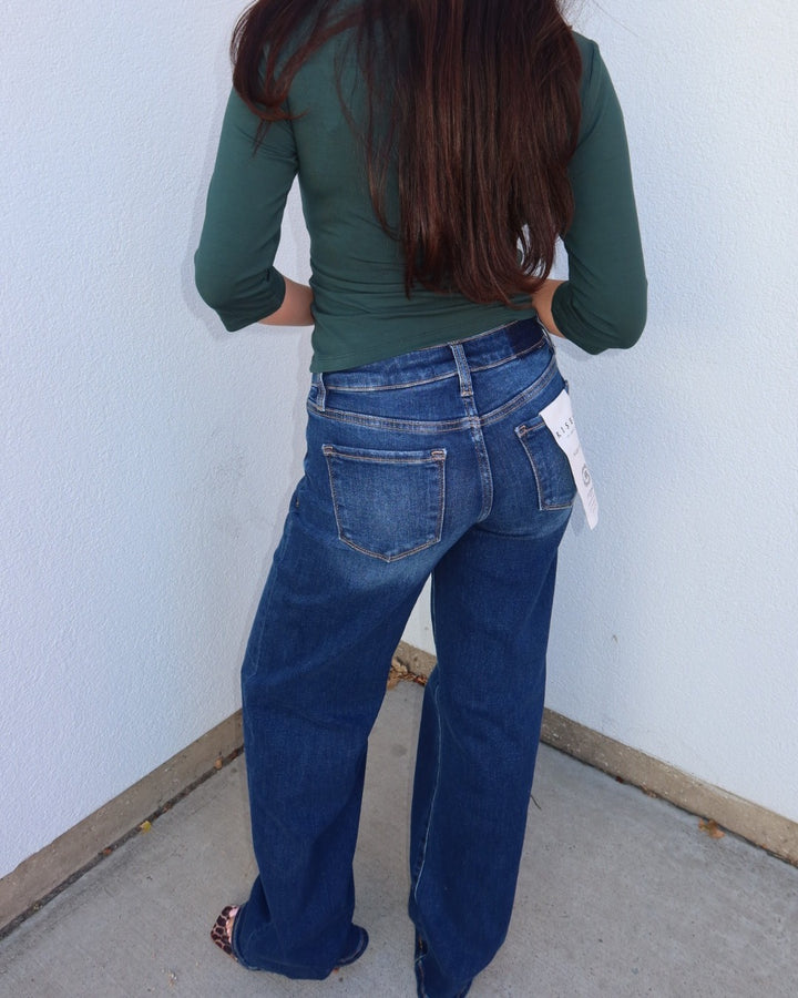 Back view of the Waltman low rise dark wash wide leg jeans with a green top, hang tag on the back pocket