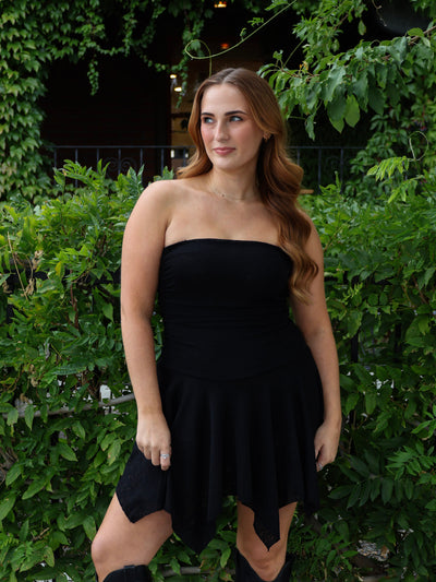 Woman wearing a black strapless dress standing in front of green foliage