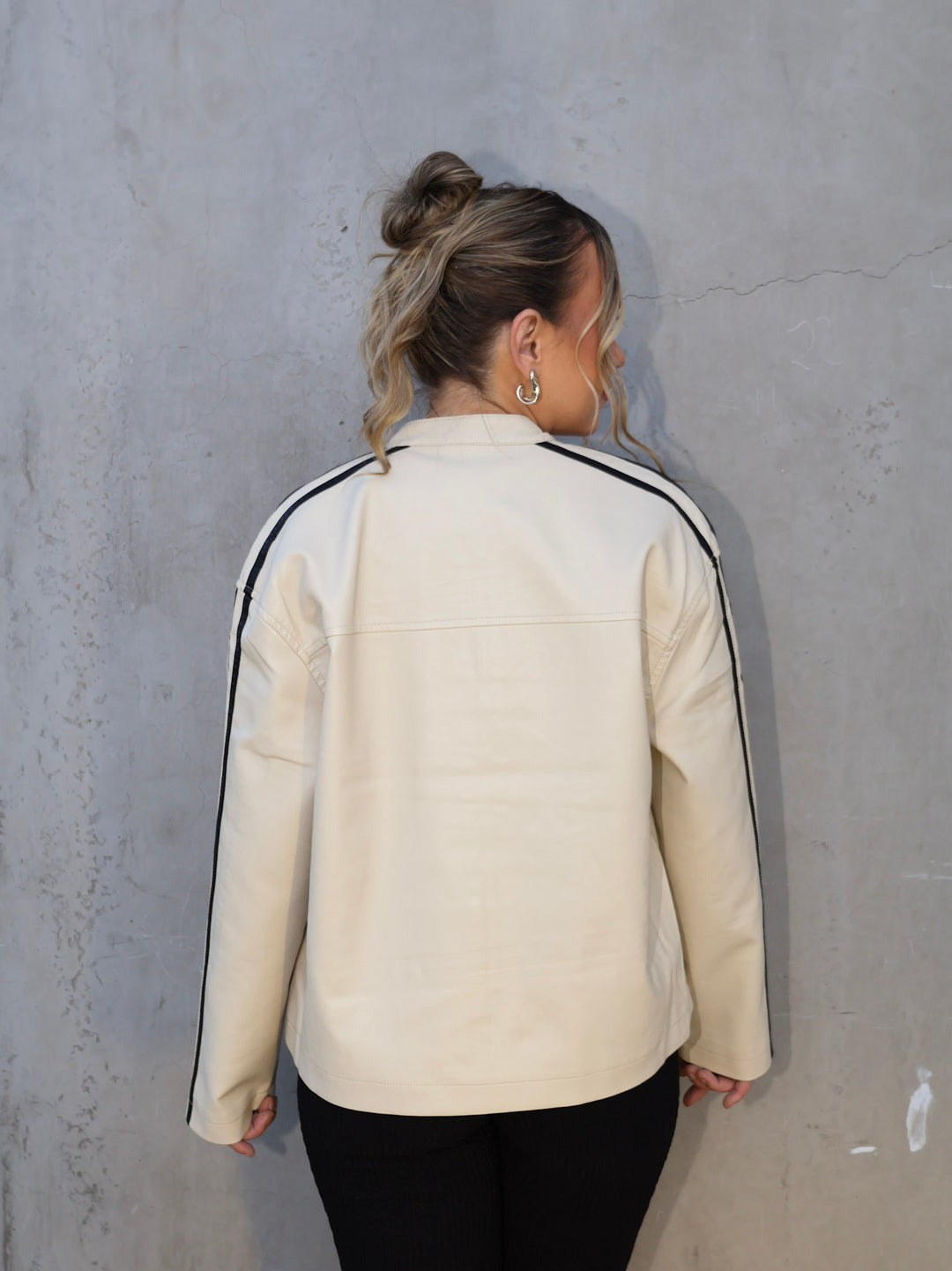 Person wearing a cream-colored jacket with black stripes on a gray wall
