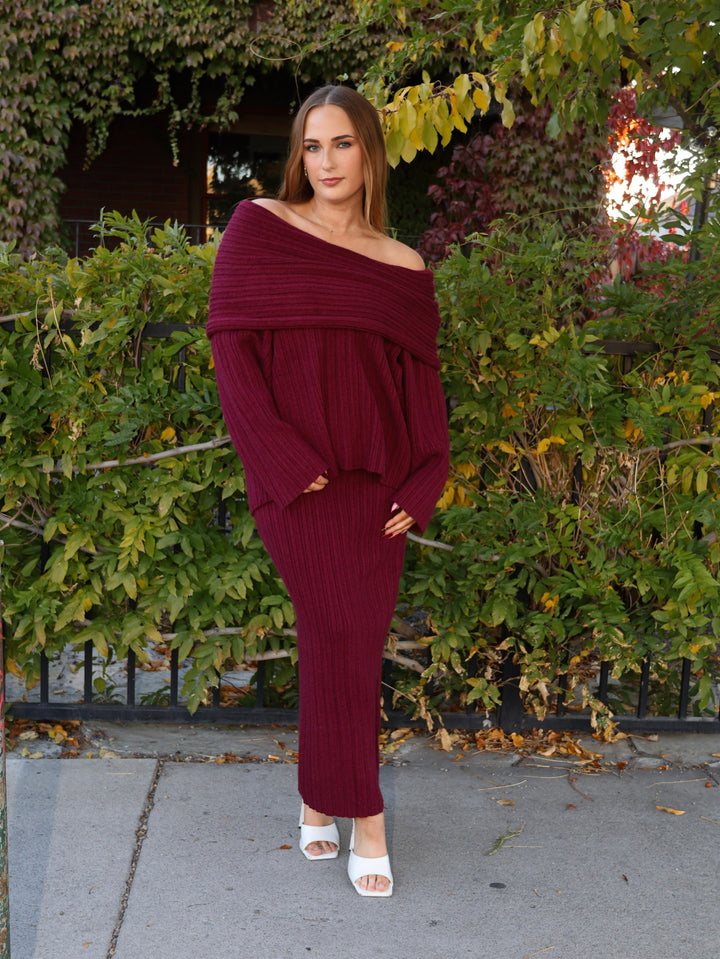 Woman wearing a burgundy off-shoulder sweater and skirt standing outdoors.
