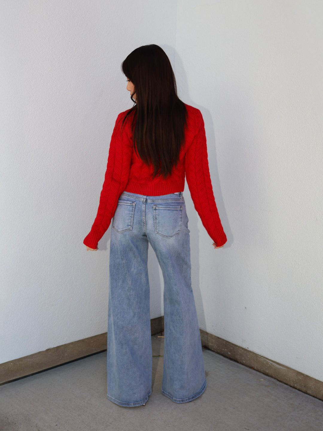 Person wearing a red shirt and blue jeans standing against a white wall.