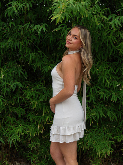 Woman in a white dress standing against a green leafy background