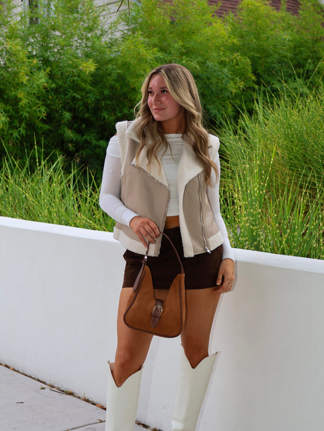 Woman in a casual outfit with a vest, shorts, and white boots standing outdoors.