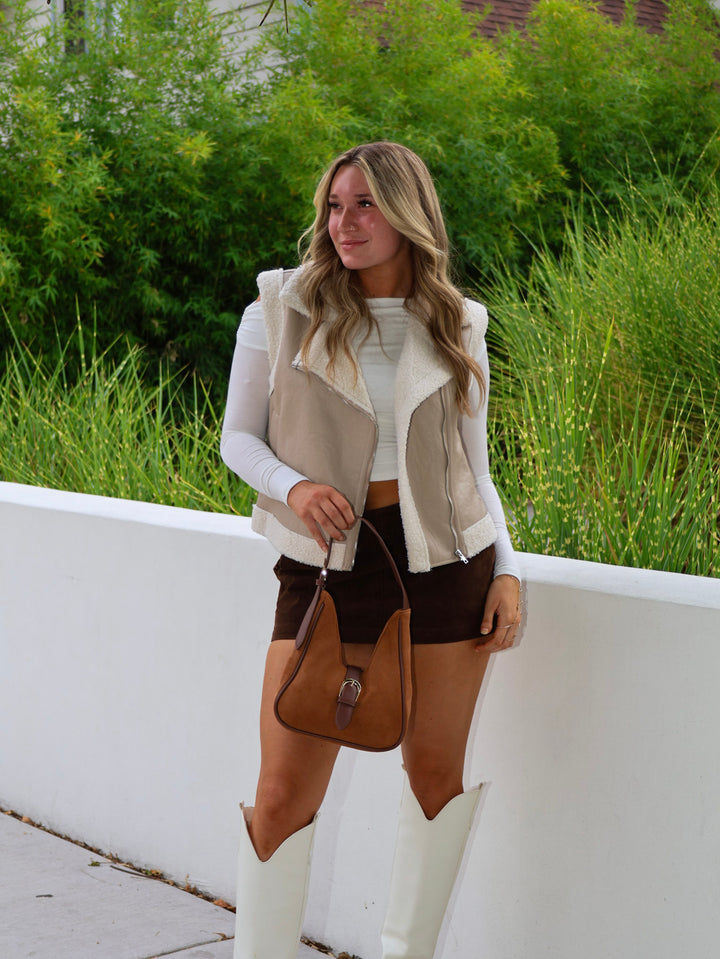 Woman in a casual outfit with a vest, shorts, and white boots standing outdoors.