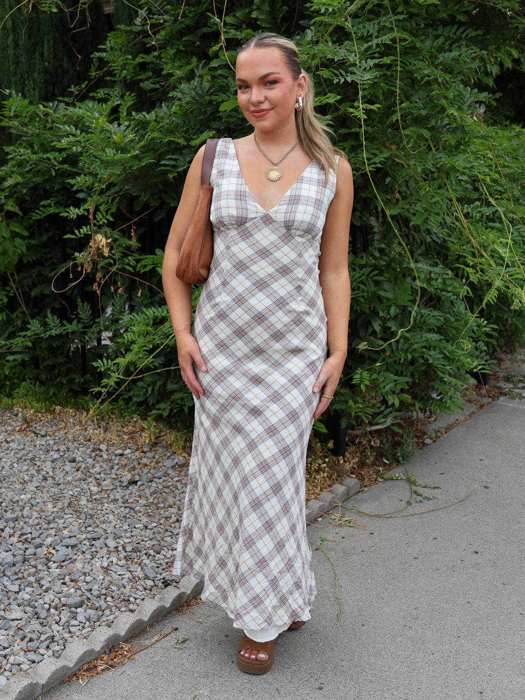 Woman in a plaid dress standing outdoors with greenery in the background