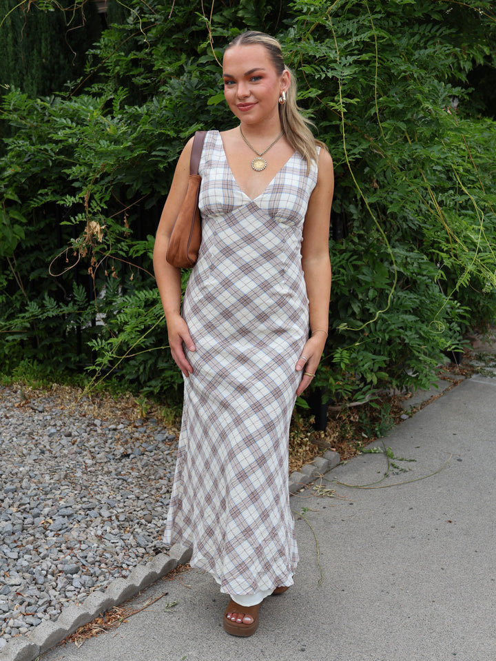 Woman in a plaid dress standing outdoors with greenery in the background