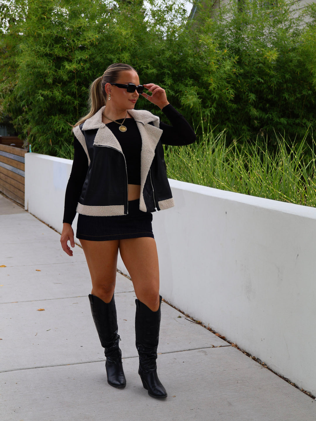 Woman wearing a black and white jacket, black skirt, and black knee-high boots outdoors.