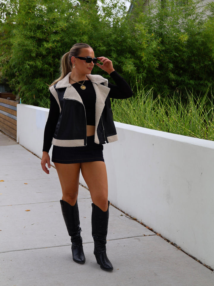 Woman wearing a black and white jacket, black skirt, and black knee-high boots outdoors.
