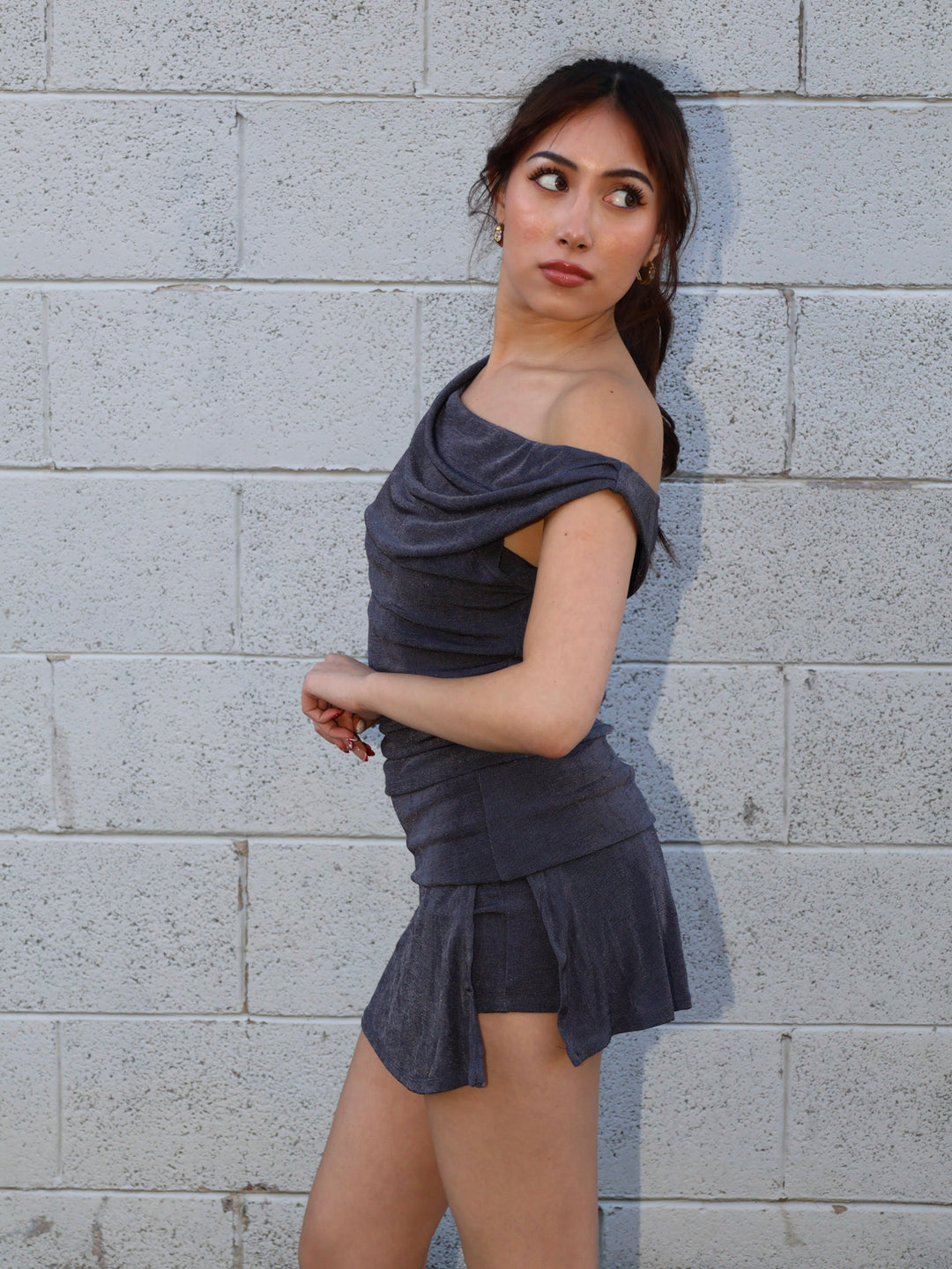 Woman wearing a gray off-shoulder dress against a gray brick wall