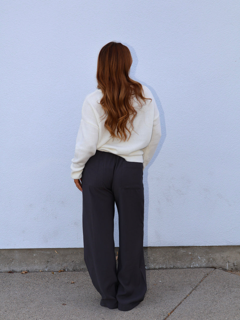 Person wearing a white sweater and dark pants against a light blue wall.
