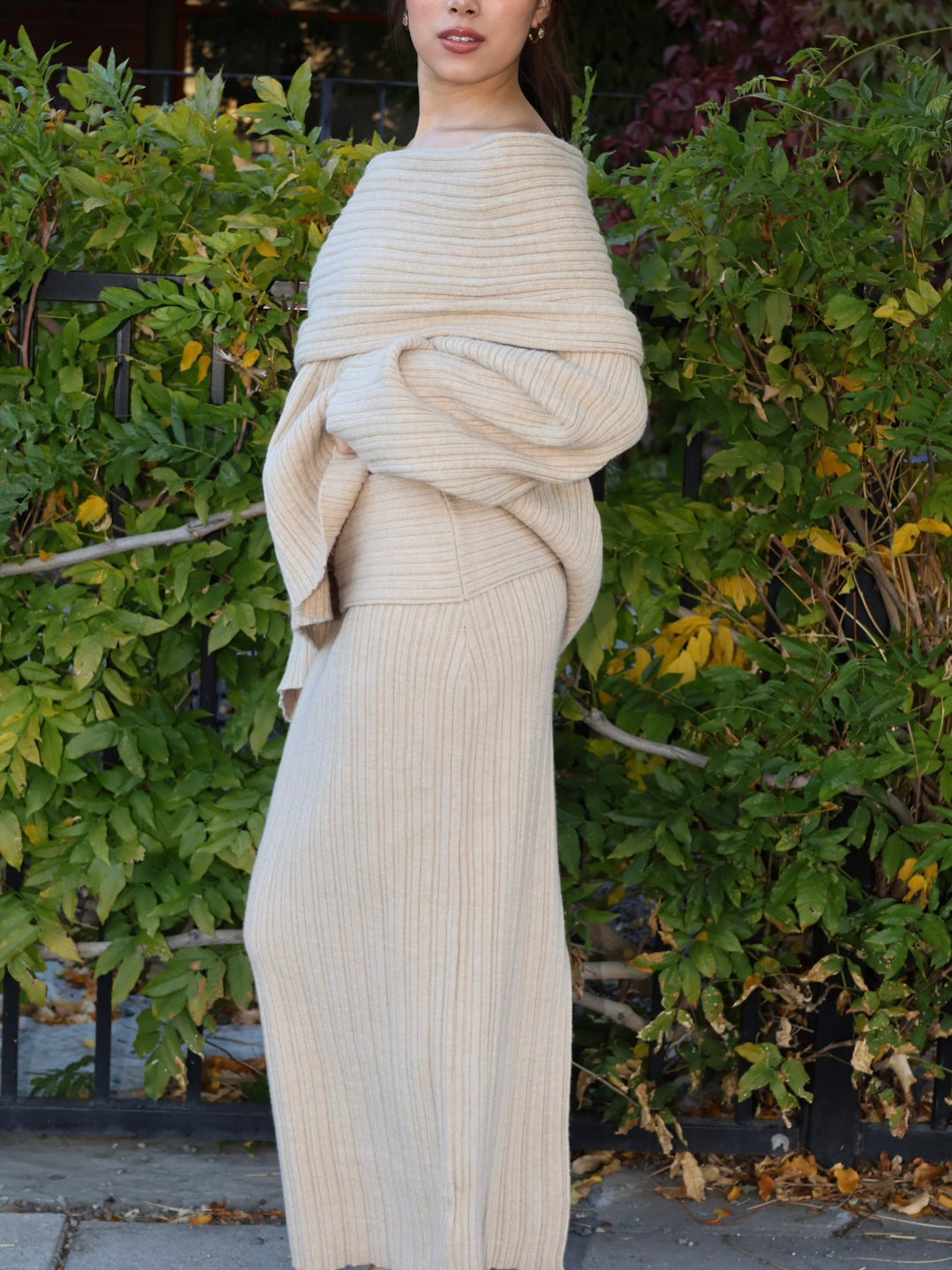 Person wearing a beige ribbed knit outfit standing outdoors with greenery in the background