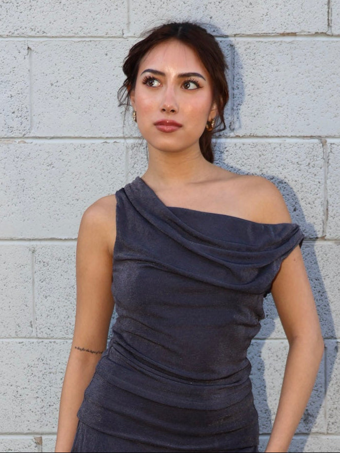 Woman wearing a dark blue off-shoulder top against a light gray brick wall.