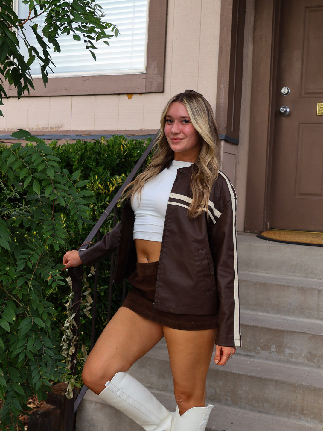 Woman in a brown and white outfit standing on steps outside a house.