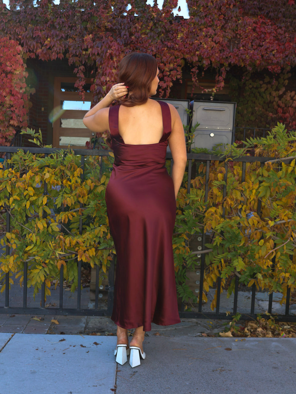 Woman in a burgundy dress standing in front of a house with autumn foliage.