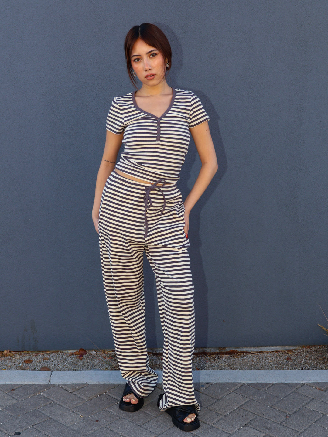 Woman wearing a gray and white striped jumpsuit standing against a gray wall.