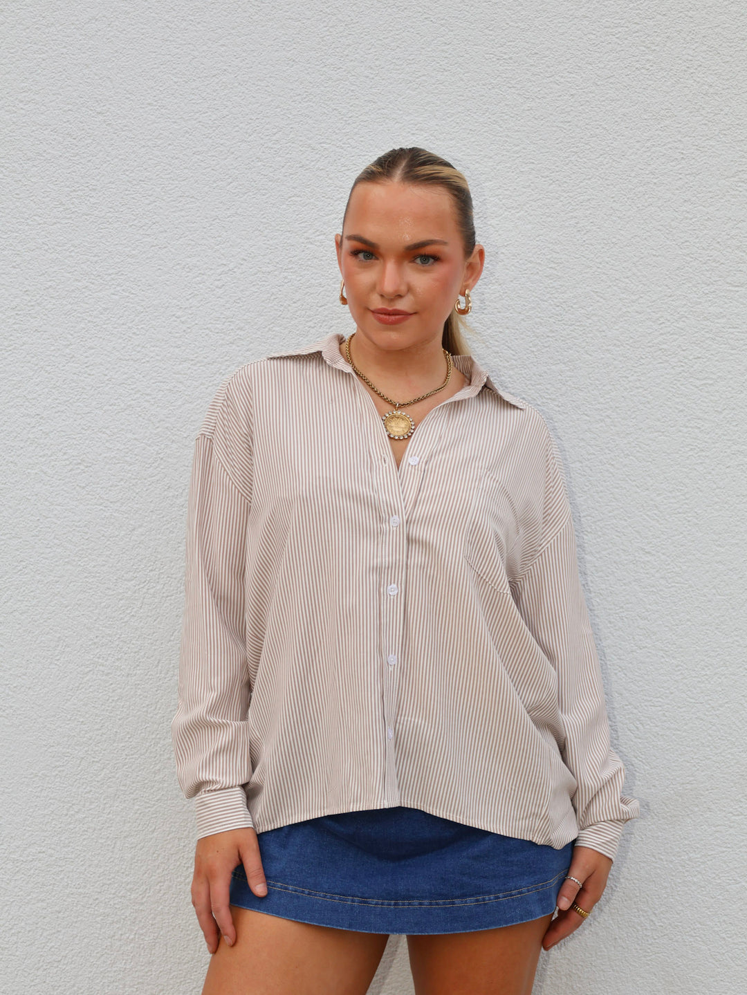 Woman wearing a beige striped shirt and blue shorts against a light gray background