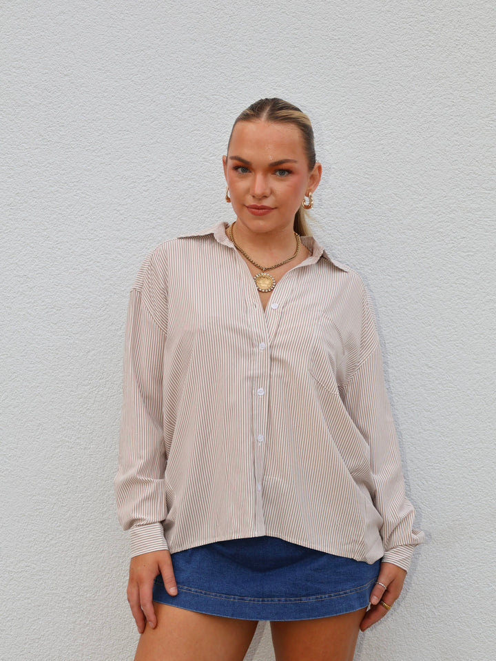 Woman wearing a beige striped shirt and blue shorts against a light gray background