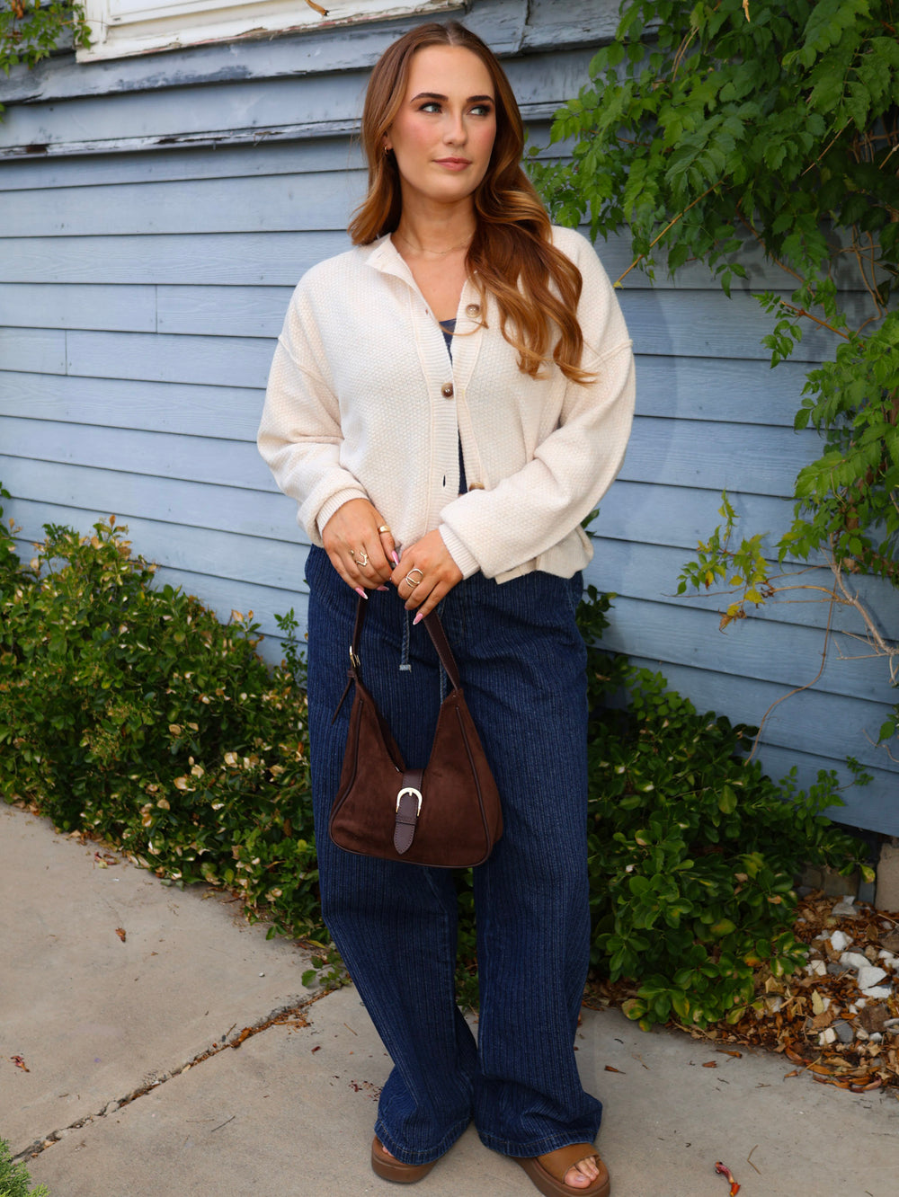 Woman in a white shirt and blue jeans standing outdoors against a blue wall.