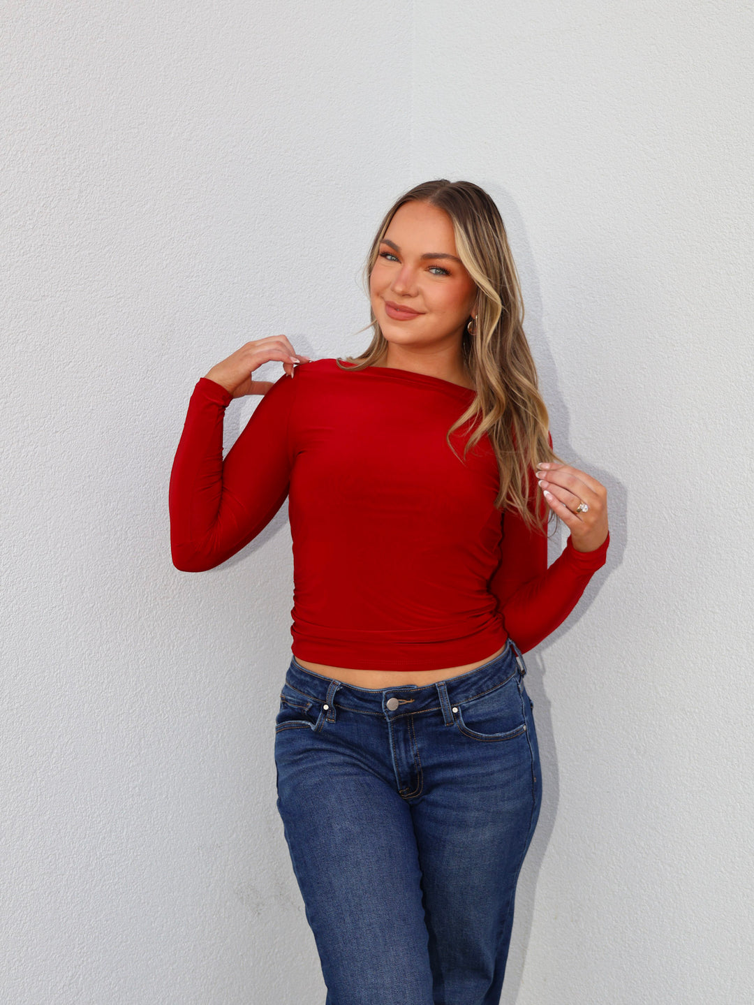 Woman wearing a red long-sleeve top and blue jeans against a white background