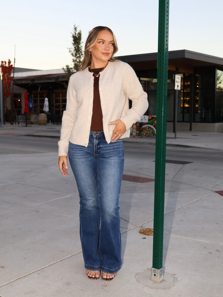 Woman wearing a white jacket and blue jeans standing outdoors.