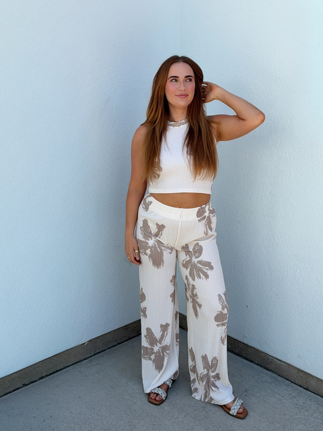 Woman wearing a white top and floral pants against a light blue wall.