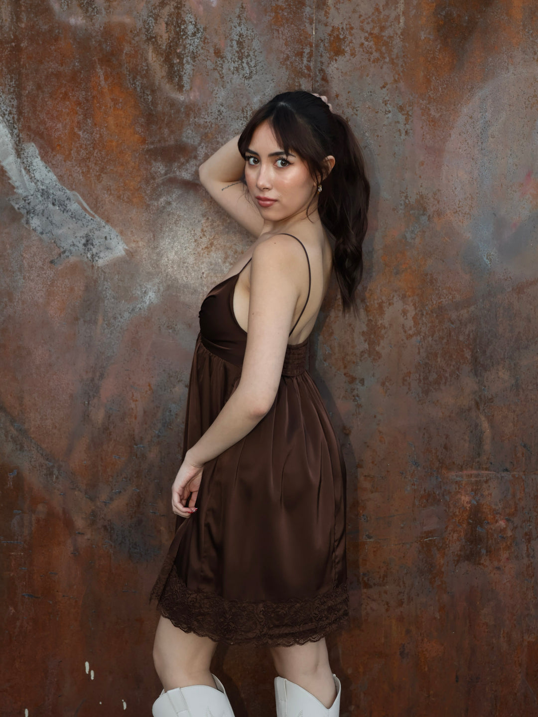 Woman in a brown dress standing against a textured brown wall