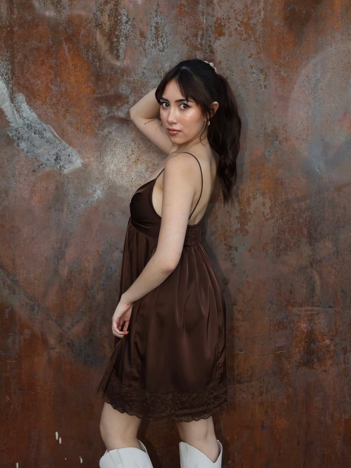 Woman in a brown dress standing against a textured brown wall