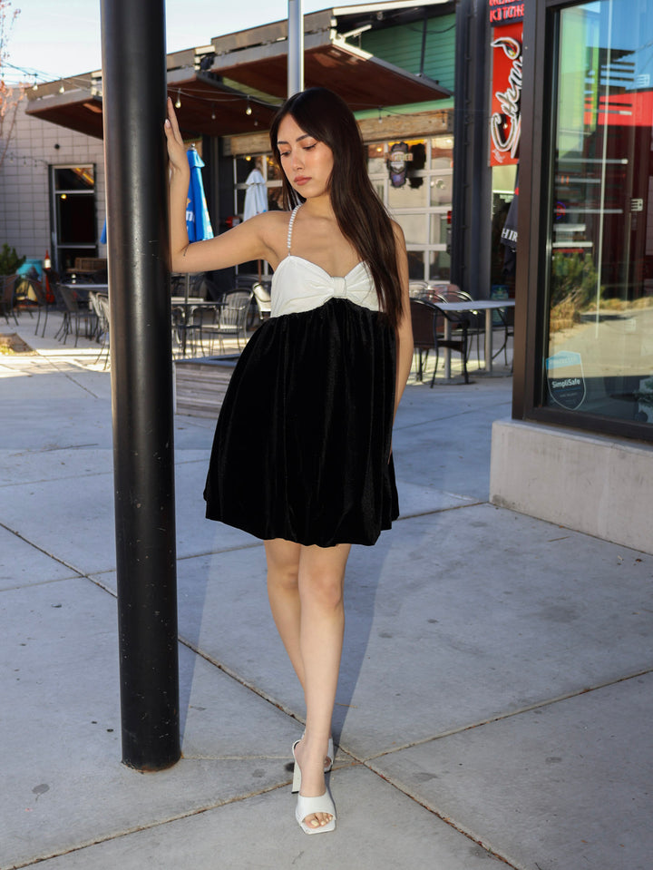 Woman in a black and white dress standing on a sidewalk with a building in the background