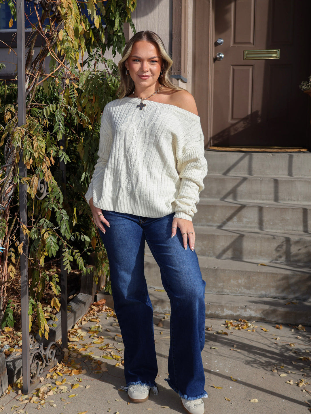 Woman wearing a white sweater and blue jeans standing on steps outside a house.
