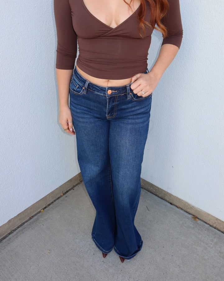 Front close-up of the Waltman low rise dark wash wide leg jeans with a brown top, hand at the pocket