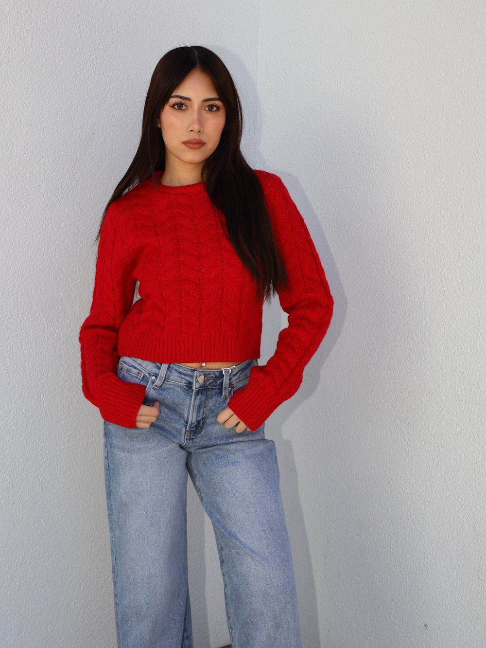 Woman wearing a red sweater and blue jeans against a plain background