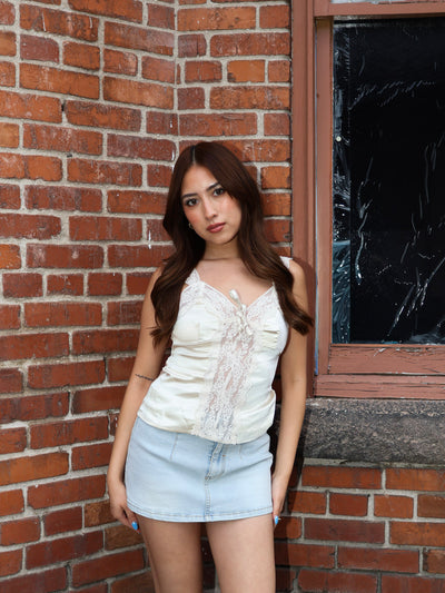 Woman in a white top and light blue shorts standing against a brick wall.