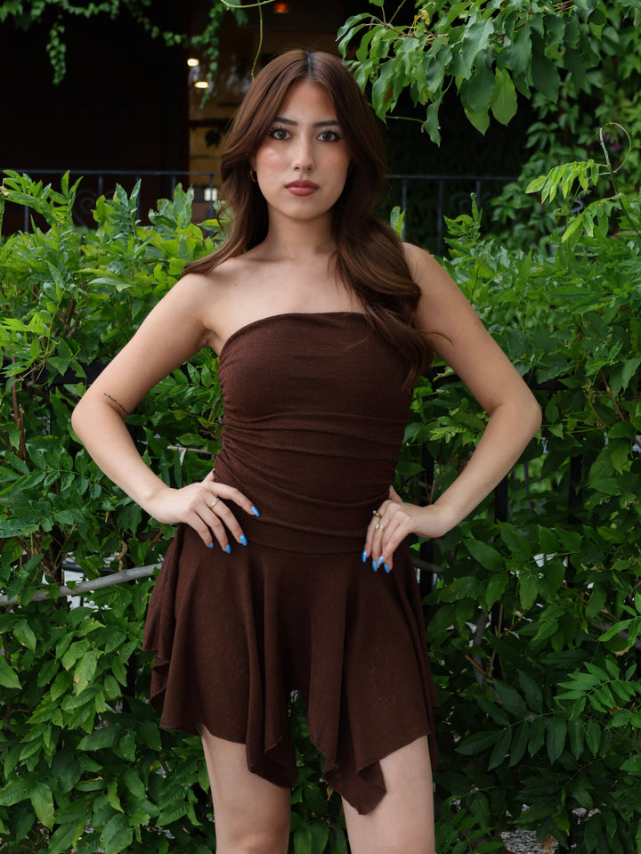 Woman wearing a brown strapless dress standing in front of green foliage