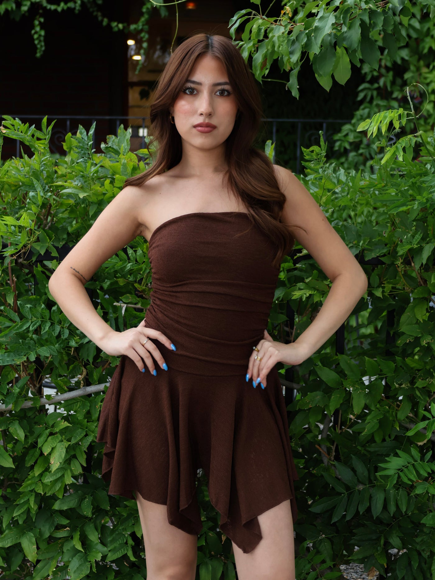 Woman wearing a brown strapless dress standing in front of green foliage