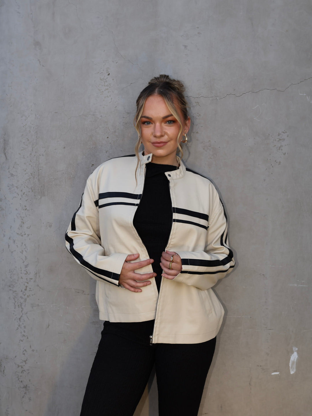 Woman wearing a cream jacket with black stripes against a gray wall