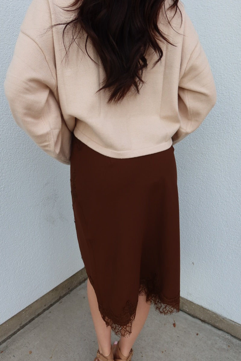 Close back view of the brown Lucy asymmetric lace trim satin midi skirt, showing the lace hem and slit