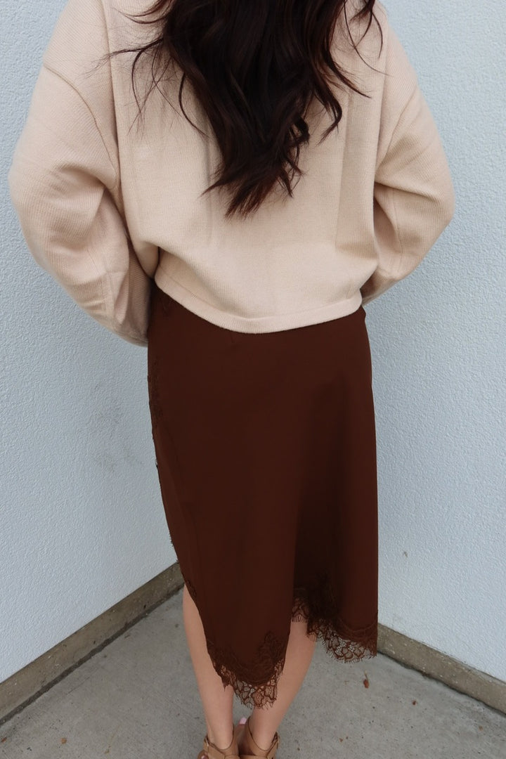 Close back view of the brown Lucy asymmetric lace trim satin midi skirt, showing the lace hem and slit