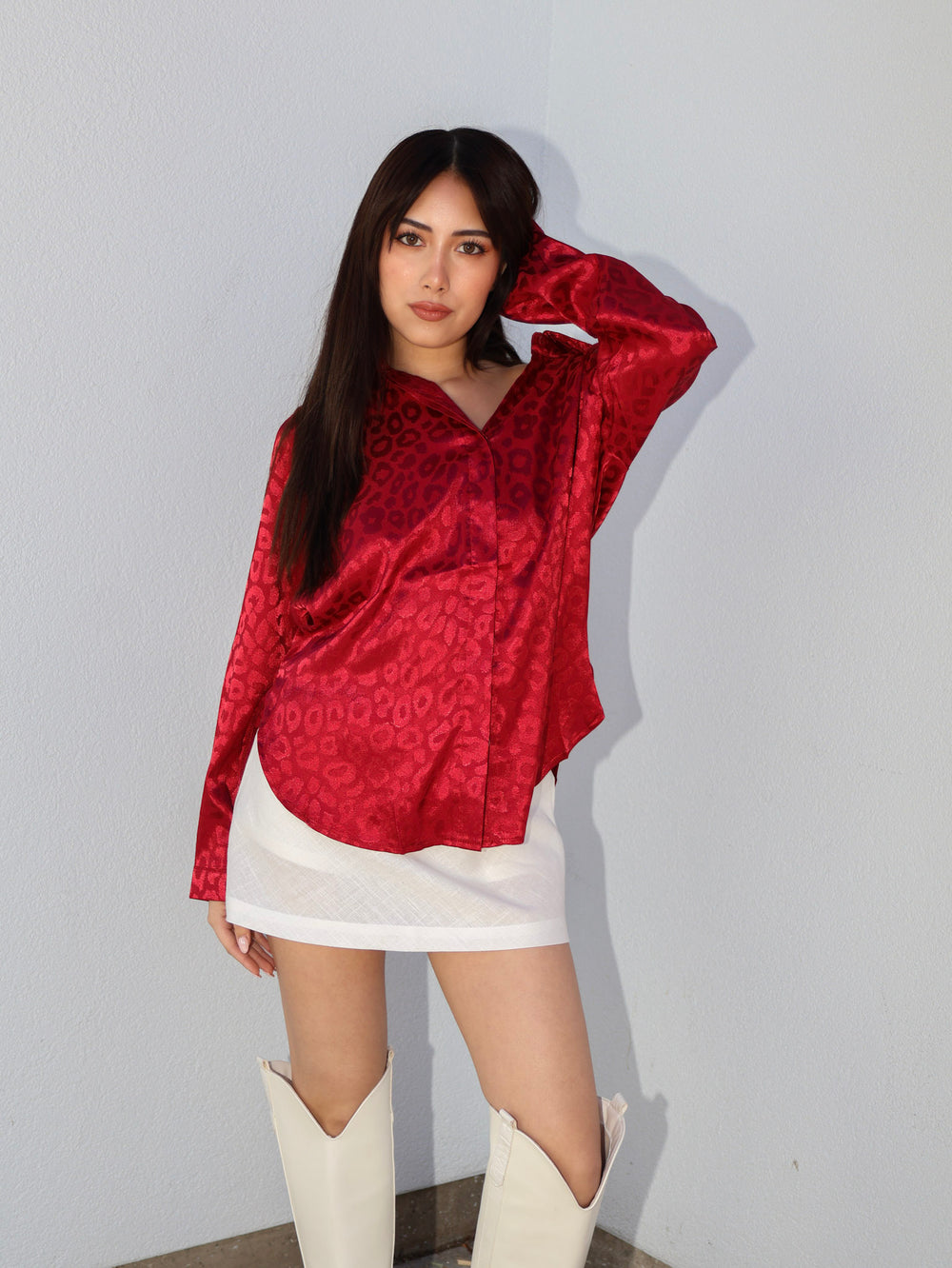 Woman wearing a red patterned blouse and white skirt with high boots against a plain background