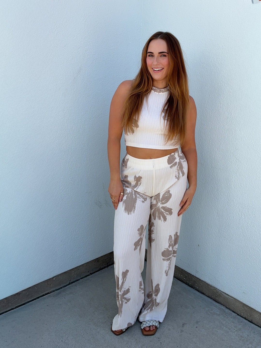 Woman wearing a white top and floral pants against a light blue wall.