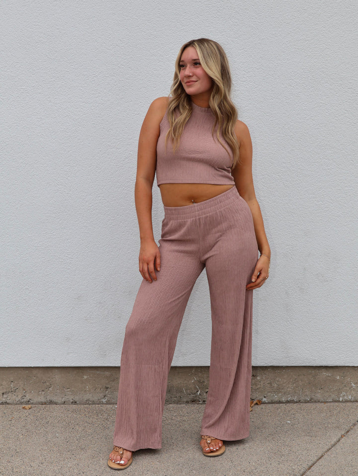 Woman wearing a matching pink top and pants set against a white wall.