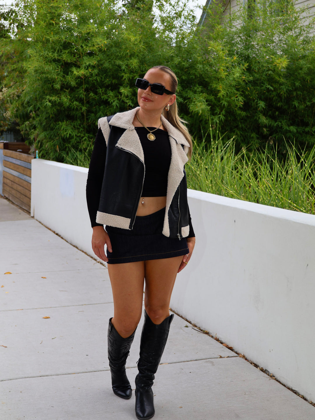 Woman wearing a black and white jacket, black top, skirt, and boots outdoors.
