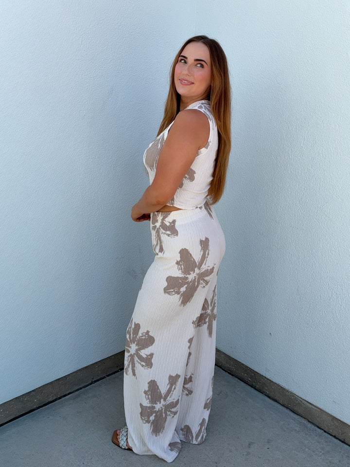 Woman wearing a white dress with brown floral patterns against a light blue wall.