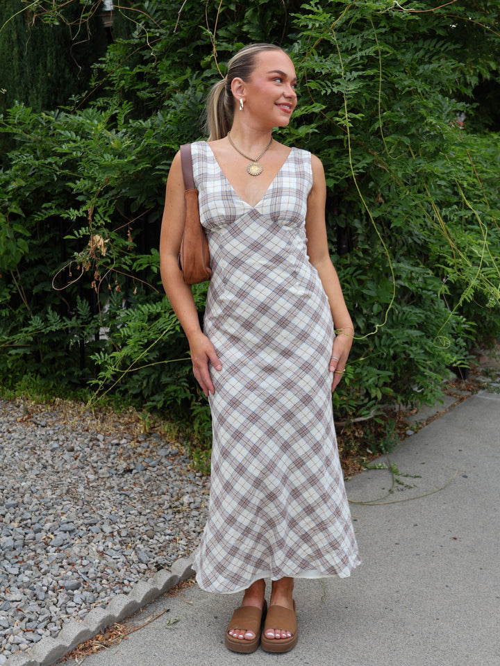 Woman wearing a plaid dress standing outdoors with greenery in the background