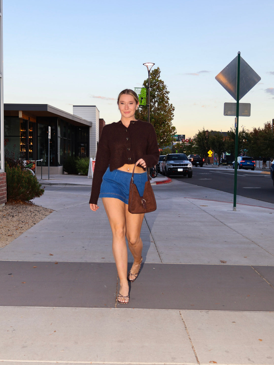 Woman walking on a sidewalk in an urban setting with buildings and street signs in the background.