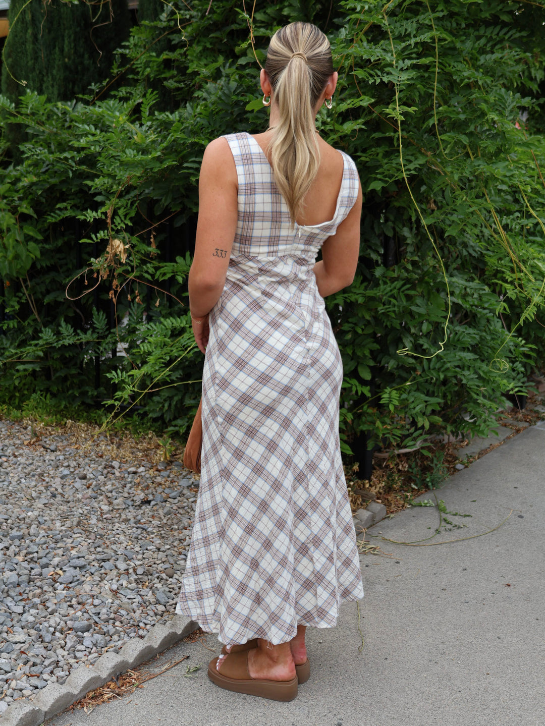 Woman in a plaid dress walking away from the camera with greenery in the background
